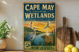 A vintage-style sign for Cape May Coastal Wetlands, New Jersey, featuring a seagull, lighthouse, and a sunset landscape.