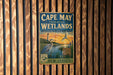 A vintage-style metal sign for Cape May Coastal Wetlands, New Jersey, featuring an illustration of a bird and a lighthouse.