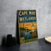 A vintage-style metal sign for Cape May Coastal Wetlands, New Jersey, featuring an illustration of a bird and a lighthouse.