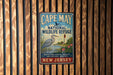 A vintage metal sign for Cape May National Wildlife Refuge, featuring a blue heron and a lighthouse, is displayed on a wooden fence.
