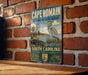 A vintage-style sign for the Cape Romain National Wildlife Refuge in South Carolina, featuring an illustration of a crane and a lighthouse.