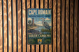 A vintage metal sign for the Cape Romain National Wildlife Refuge in South Carolina, featuring a lighthouse and a bird, is displayed on a wooden wall.
