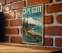 A vintage-style metal sign for Cape Scott Provincial Park in British Columbia, Canada, featuring a scenic landscape with a beach, mountains, and a body of water.