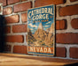 A vintage-style metal sign for Cathedral Gorge State Park in Nevada, featuring a mountain landscape and the text "Cathedral Gorge State Park" and " Nevada" on it.