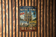 A vintage metal sign featuring the Notre-Dame Cathedral in Paris, France, with text and images of the cathedral and surrounding area.