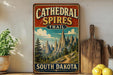 A vintage-style sign for the Cathedral Spires Trail in South Dakota, featuring a scenic mountain landscape.