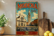 A vintage-style metal sign with the text "MODENA Italia" and an illustration of a church and a clock tower, placed on a shelf next to a wooden cutting board and some lemons.