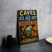 A vintage-style metal sign with the text "CAVES and ICE AGE ART in the SWABIAN JURA" and an illustration of a cave with a horse, placed on a gray countertop next to some black camera lenses.