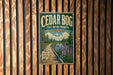 A vintage-style sign for Cedar Bog State Nature Preserve in Ohio, featuring a scenic image of a wooden boardwalk leading to a lake surrounded by trees and flowers.