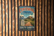 A vintage metal sign for the Centennial Trail in South Dakota, featuring a scenic mountain landscape and the trail's name.