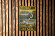 a vintage metal sign with a colorful illustration of a landscape, including a waterfall, an ostrich, and a bird, mounted on a wooden wall.