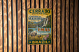 a vintage metal sign with a colorful illustration of a landscape, including a waterfall, an ostrich, and a bird, mounted on a wooden wall.
