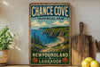 A vintage-style sign for Chance Cove Provincial Park, New Brunswick and Labrador, featuring a scenic coastal landscape with cliffs, a beach, and a blue ocean.