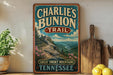 A vintage-style metal sign for Charlie's Bunion Trail in Tennessee, featuring a scenic mountain landscape with pine trees and mountains.