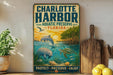 A vintage-style sign for Charlotte Harbor Aquatic Preserve in Florida, featuring illustrations of marine life such as a dolphin, manatee, and turtle, along with a sunset and palm trees.