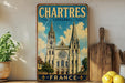 A vintage-style metal sign displaying the name "CHARTRES CATHEDRAL FRANCE" with an illustration of the Chartres Cathedral in the background.
