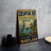 A vintage metal sign for Chesapeake Bay National Estuarine Research Reserve, featuring an illustration of a heron and a lighthouse, is displayed on a gray countertop next to some black camera lenses.