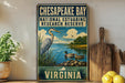 A vintage-style metal sign for Chesapeake Bay National Estuarine Research Reserve, featuring an illustration of a heron and ducks in the water, with the text "CHESAPEAKE BAY VIRGINIA" and "NATIONAL ESTUARINE RESEARCH RESERVE".