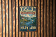 A vintage metal sign for Chesapeake Bay Watershed Cultural Landscape, featuring a scenic illustration of a coastal landscape with a river, house, and sailboat.