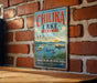A vintage metal sign with the text "CHILIKA LAKE INDIA" is hanging on a brick wall.
