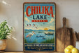 A vintage-style sign for Chilika Lake, India, featuring a serene landscape with birds, boats, and a sunset.