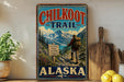 A vintage-style metal sign for the Chilkoot Trail in Alaska, featuring a hiker and scenic mountain landscape.