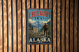A vintage metal sign for the Chilko Trail in Alaska, featuring a hiker and a scenic mountain landscape.