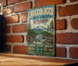 A vintage-style metal sign for Choccolocco State Forest in Alabama, featuring a scenic illustration of a mountain, river, and forest.