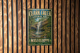 A vintage metal sign for Clark Creek Natural Area in Mississippi, featuring a waterfall and lush greenery.