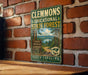 A metal sign with a scenic forest landscape and the text "CLEMMONS EDUCATIONAL STATE FOREST NORTH CAROLINA" is displayed on a brick wall.