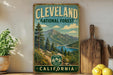 A vintage-style metal sign for Cleveland National Forest, featuring a scenic mountain landscape with a lake and pine trees.