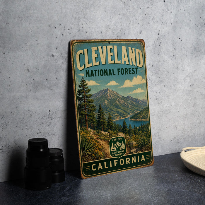 A vintage-style metal sign for Cleveland National Forest, featuring a scenic mountain landscape with pine trees and a lake.
