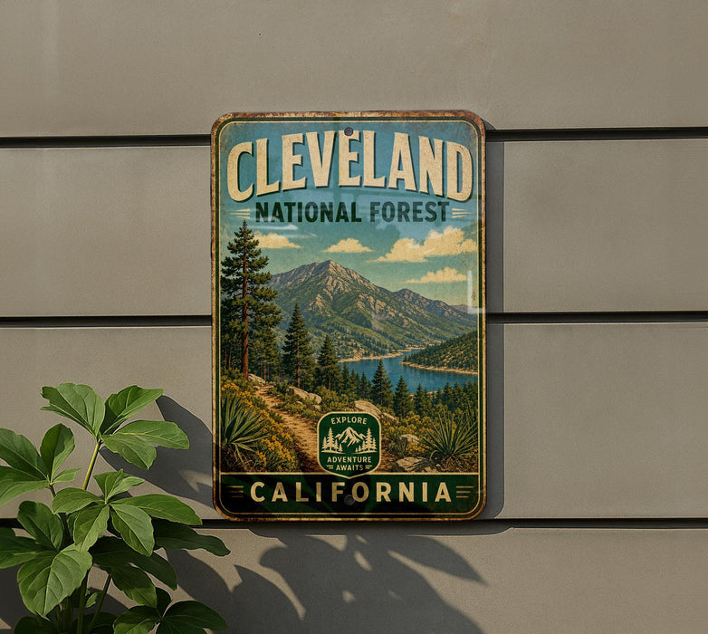A vintage metal sign for Cleveland National Forest, featuring a scenic mountain landscape with pine trees and a lake, mounted on a wall.