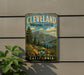A vintage metal sign for Cleveland National Forest, featuring a scenic mountain landscape with pine trees and a lake, mounted on a wall.