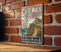 A vintage-style metal sign for Cliff Walk, Rhode Island, mounted on a brick wall.