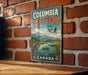 A vintage-style sign for Columbia Wetlands, a wildlife sanctuary in Canada, featuring a serene landscape with mountains, a lake, and various birds.