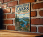 A vintage metal sign for Connecticut Lakes State Forest in New Hampshire, featuring a scenic illustration of the lake surrounded by pine trees and mountains.