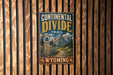 A metal sign with the text "CONTINENTAL DIVIDE TRAIL" and "WYOMING" is displayed on a wooden wall.