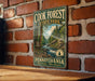A vintage metal sign for Cook Forest State Park in Pennsylvania, featuring a scenic illustration of a forest and a river.