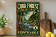 A vintage-style sign for Cook Forest State Park in Pennsylvania, featuring a scenic image of a forest and a river.