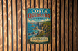 A vintage metal sign for Costaque Park in Cantaerre, Spain, featuring a coastal landscape with cliffs and the ocean.