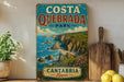A vintage-style sign for Costa Quedbrada Park in Cantabria, Spain, featuring a scenic coastal landscape with cliffs and the ocean.