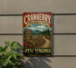 A vintage-style metal sign for the Cranberry Wilderness Trail in West Virginia, featuring a scenic landscape with a winding path, cherry blossoms, and a mountain backdrop.