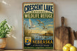 A vintage-style metal sign for the Crescent Lake National Wildlife Refuge in Nebraska, featuring a painting of swans and a lake.