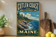 A vintage-style metal sign for Cutler Coast Public Reserve Land in Maine, featuring a scenic coastal landscape with rocky cliffs, pine trees, and the ocean.