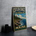 A vintage metal sign for Cutler Coast Public Reserve Land, featuring a scenic coastal landscape with rocky cliffs, pine trees, and the ocean.