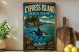 a vintage-style sign for the Cypress Island Aquatic Reserve, which is a protected and preserved natural area in Washington. The sign displays a painting of a whale swimming in the ocean, surrounded by various marine life and a scenic landscape. The sign also includes the words "Protect, Preserve, Enjoy" at the bottom, emphasizing the importance of conservation and enjoyment of the reserve.