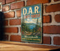 A vintage metal sign for the D.A.R. State Forest in Massachusetts, featuring a scenic landscape with pine trees, mountains, and a lake.