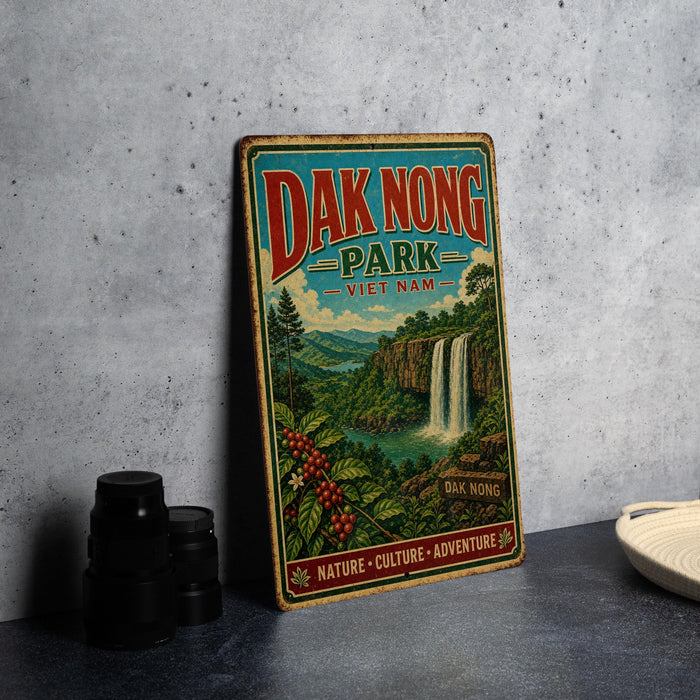 A vintage-style sign for Dak Nong Park in Vietnam, featuring a waterfall and lush greenery, is displayed on a gray concrete surface.