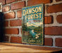 A vintage metal sign for Dawson Forest in Georgia, featuring a scenic landscape with a river and mountains, mounted on a brick wall.